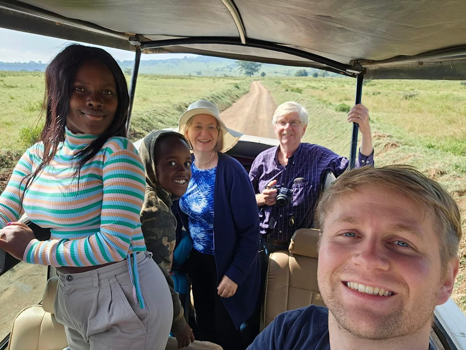 A family smiling from an open safari vehicle on a grassy track